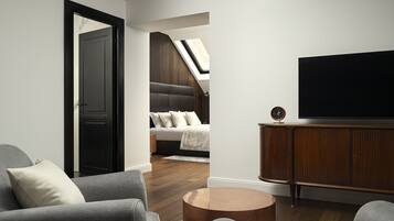 Ein modernes Wohnzimmer mit grauem Sofa, einem runden Holztisch, einem Flachbildfernseher auf einer Holzkommode und einer Treppe, die zu einer oberen Ebene führt.