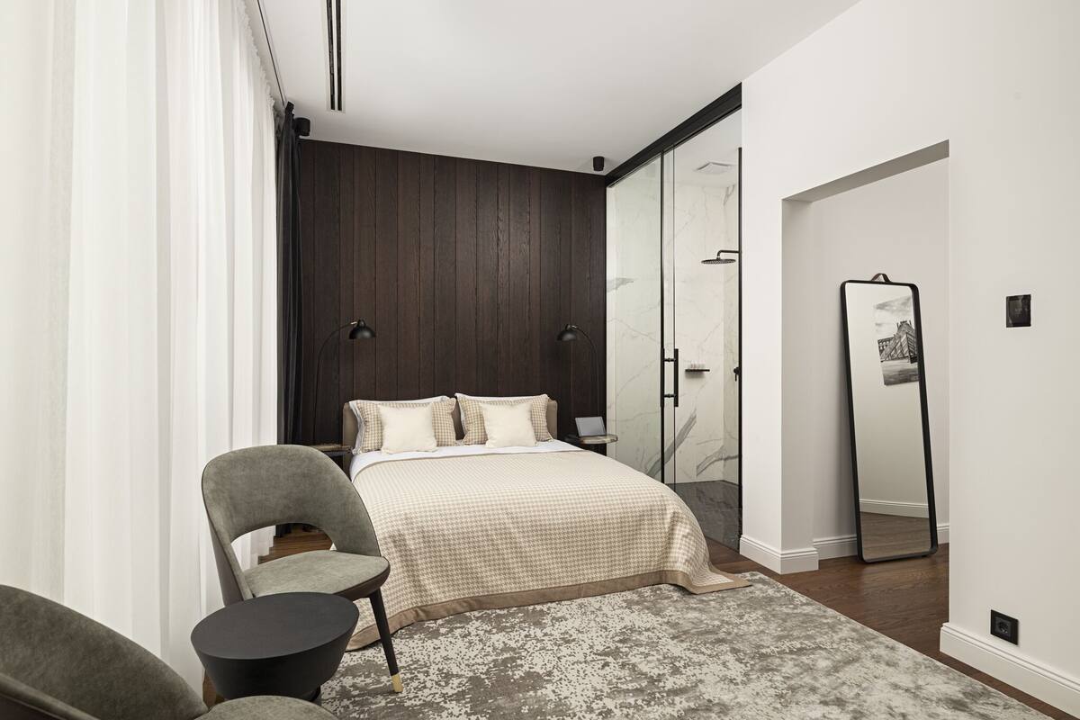 A modern bedroom with a large bed, a chair, a small table, a mirror, and a wardrobe.