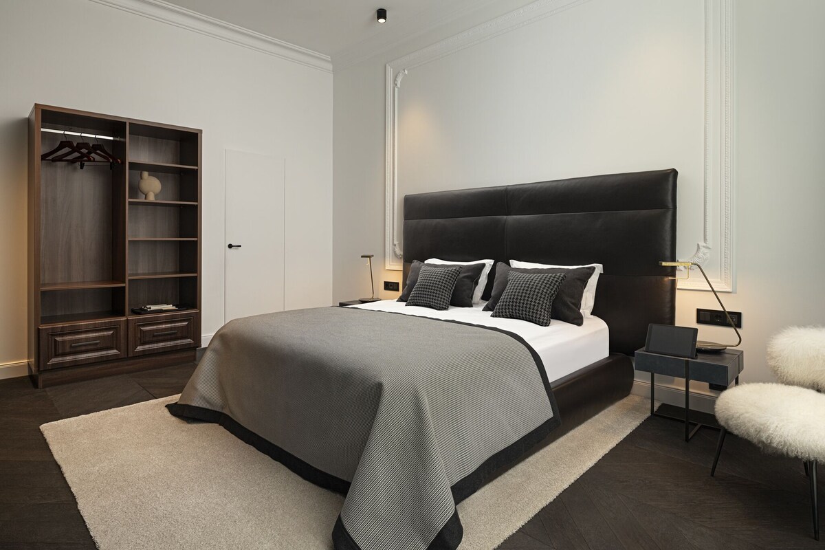 Une chambre moderne avec un grand lit, une armoire, une table de chevet avec une lampe et un fauteuil moelleux.