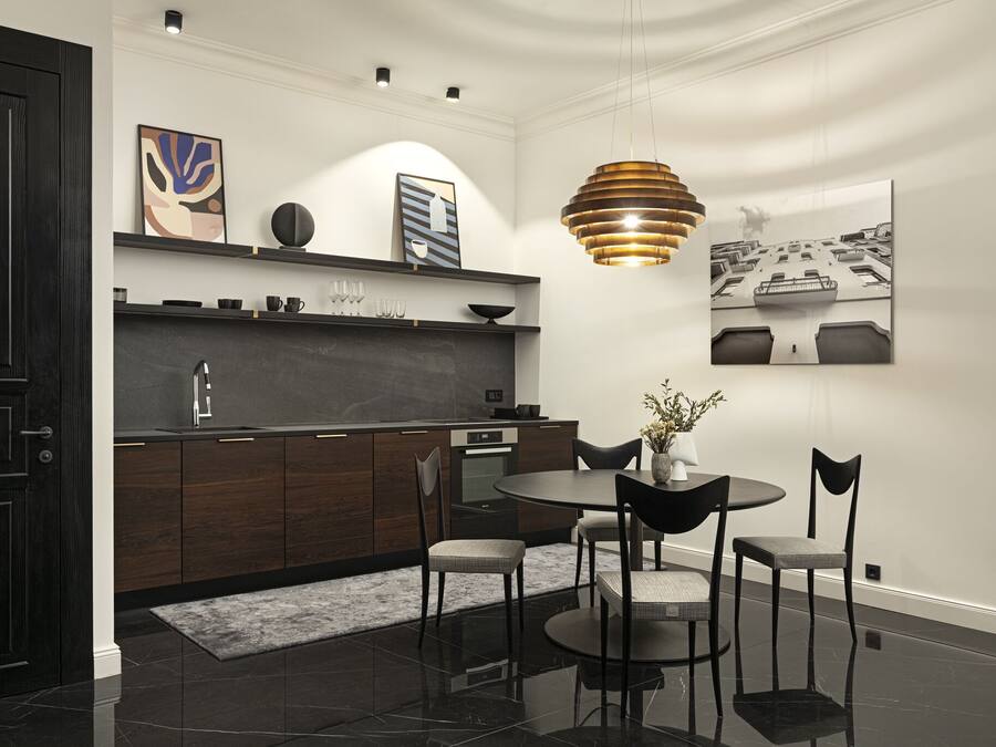 Una cocina moderna con armarios de madera oscura, encimera negra y una mesa redonda con cuatro sillas. Hay una lámpara colgante sobre la mesa y cuadros en las paredes.