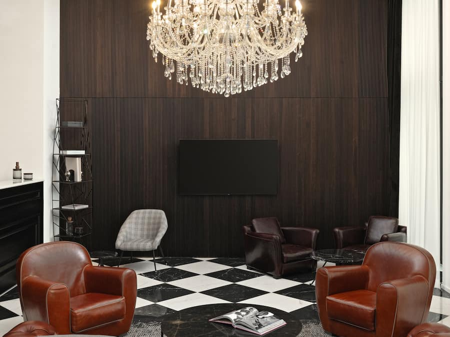 Un salón moderno con una lámpara de araña grande, sofás de cuero y un suelo a cuadros blanco y negro.