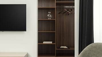 Ein modernes Zimmer mit Holzboden, einem grauen Sofa, einem Flachbildfernseher, einem Kleiderschrank mit Regalen und einem kleinen Tisch.