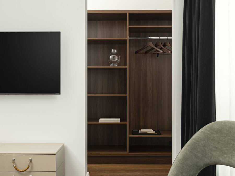 Ein modernes Zimmer mit Holzboden, einem grauen Sofa, einem Flachbildfernseher, einem Kleiderschrank mit Regalen und einem kleinen Tisch.