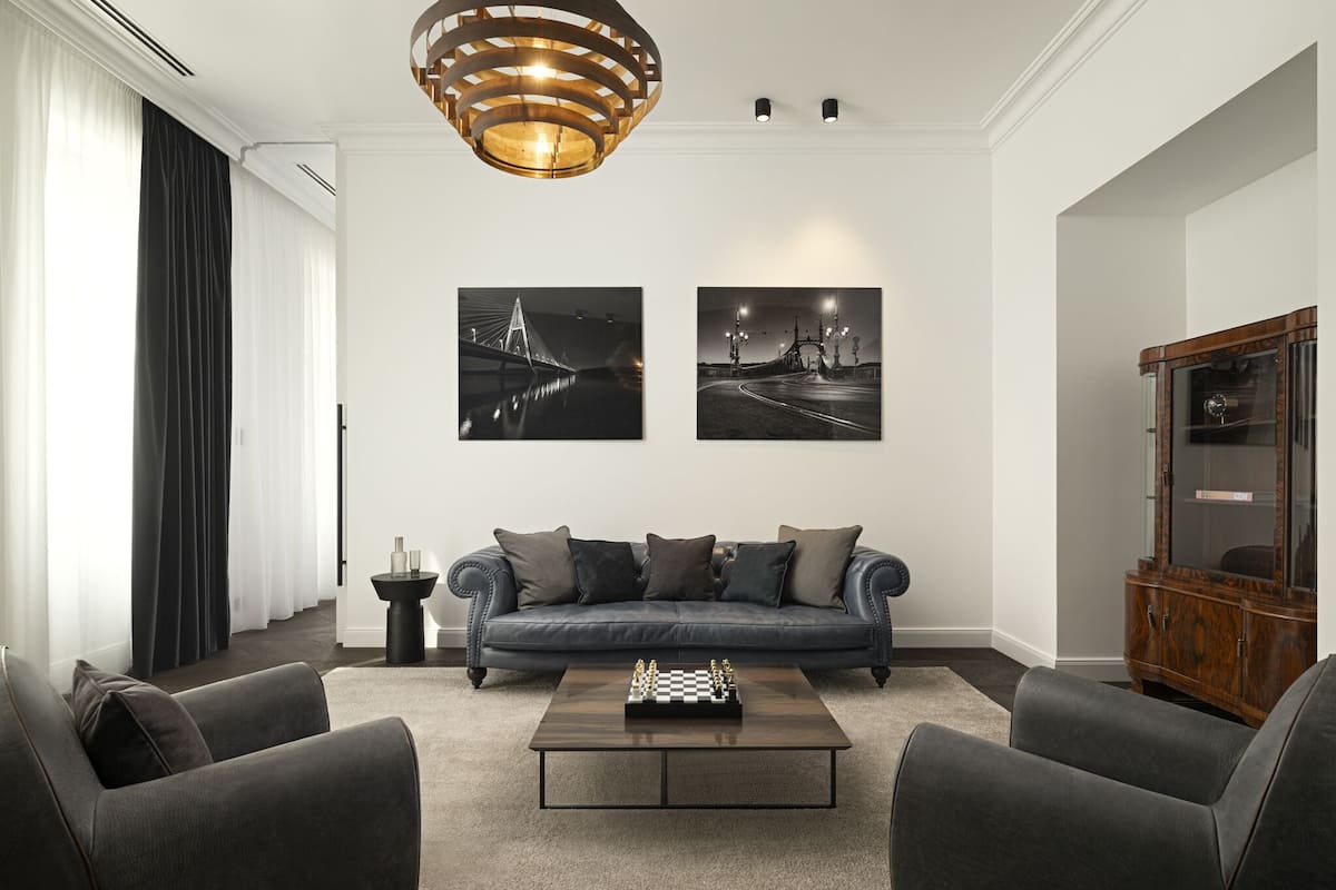 A modern living room with a dark leather sofa, a coffee table with a chess set, and two framed photographs on the wall.