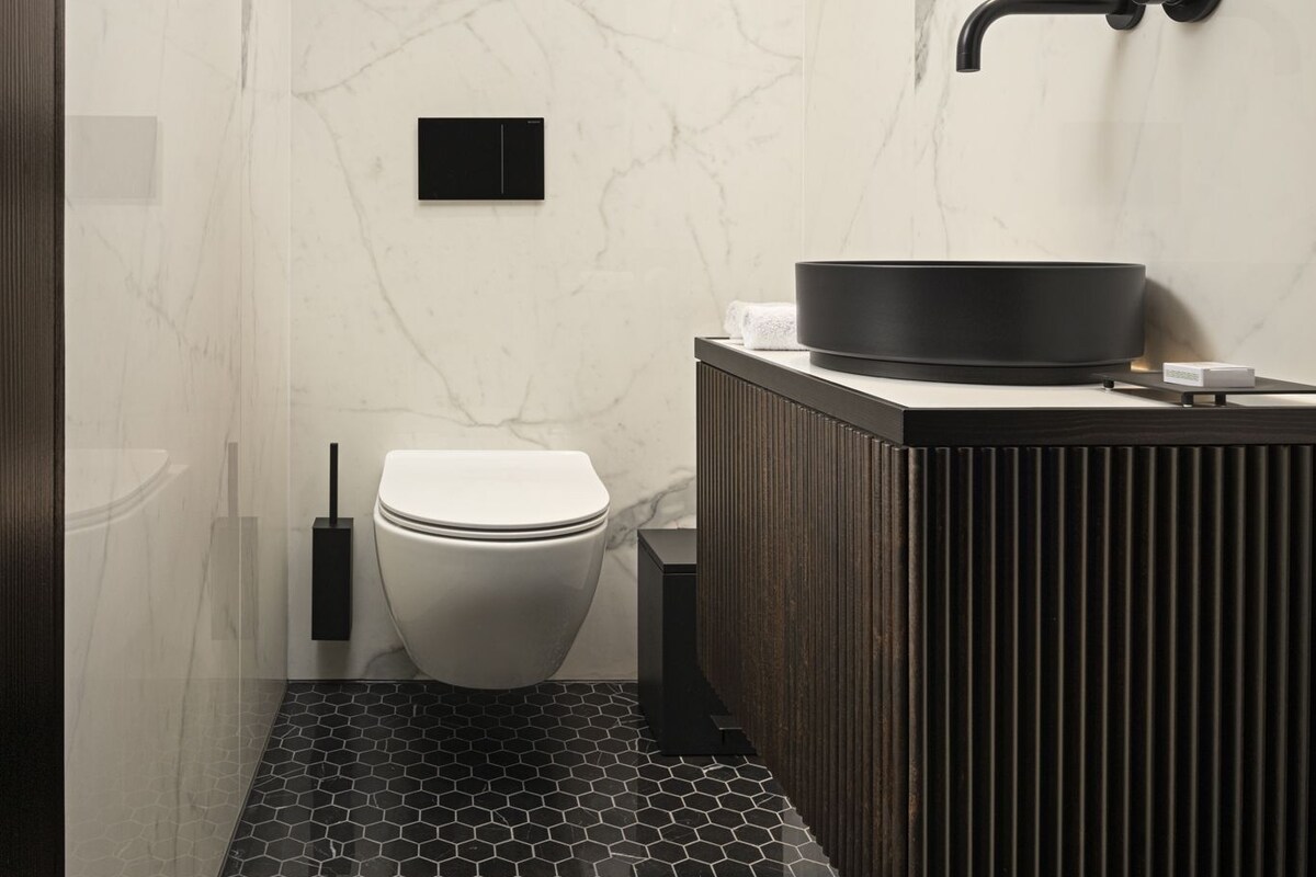 A modern bathroom with a marble wall, a black sink, and a toilet.