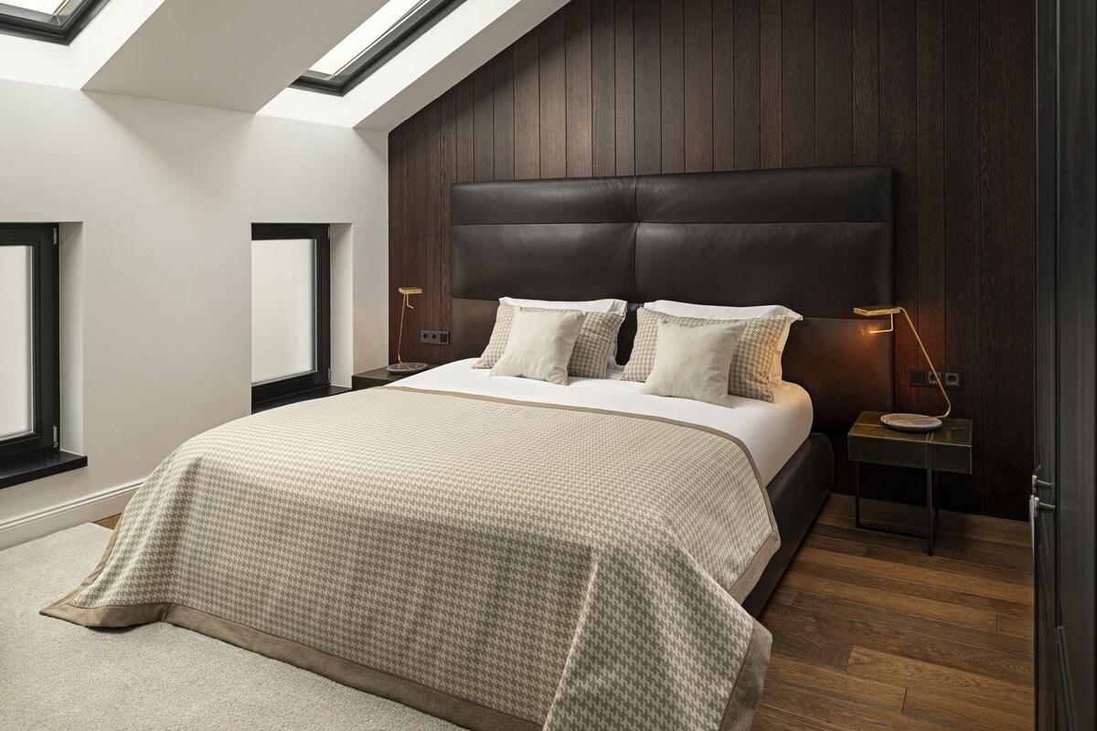 A bedroom with a large bed, wooden panel walls, a skylight, and a nightstand with a lamp.