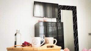 A modern room with a black cabinet, a flat-screen TV, and a wooden table with a water bottle, two mugs, and a decorative item. - Casa Perini in Chioggia (Chioggia)