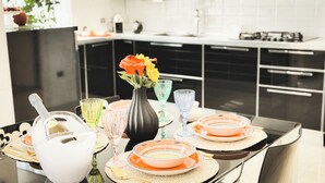 A modern kitchen with black cabinets, a white countertop, and a dining table set with colorful glassware and plates. - Casa Perini in Chioggia (Chioggia)
