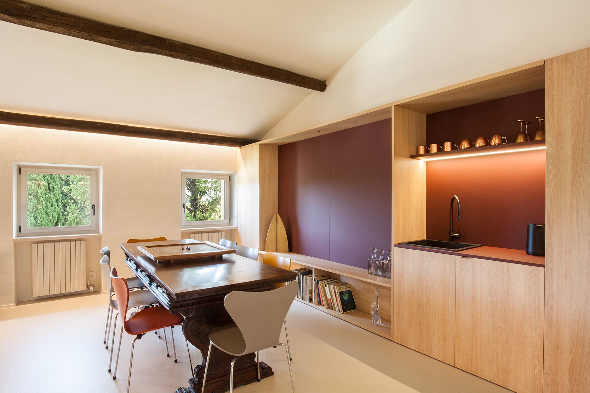 Een moderne keuken met een houten eettafel, stoelen, een inbouwboekenkast en een klein spoelgedeelte.