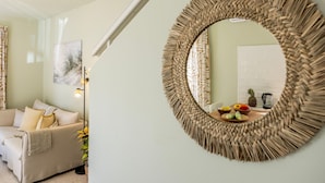 A living room with a round woven mirror, a beige sofa, and a wall-mounted artwork. - Larnaca Oneiro Seaside Villa (Pervolia)