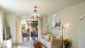 A living room with a sofa, a dining table with a fruit bowl, a TV, and a plant. - Larnaca Oneiro Seaside Villa (Pervolia)