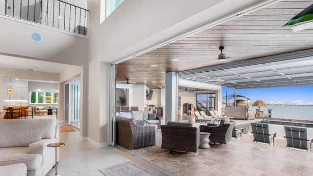 A spacious living area with a view of the water, a balcony with outdoor furniture, and a modern kitchen. - Riverfront Riviera Outdoor TV's/Hotub/Tanning Deck (Cape Coral)