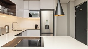 Una cuina moderna amb armaris blancs, electrodomèstics d'acer inoxidable i una làmpada penjant negra.