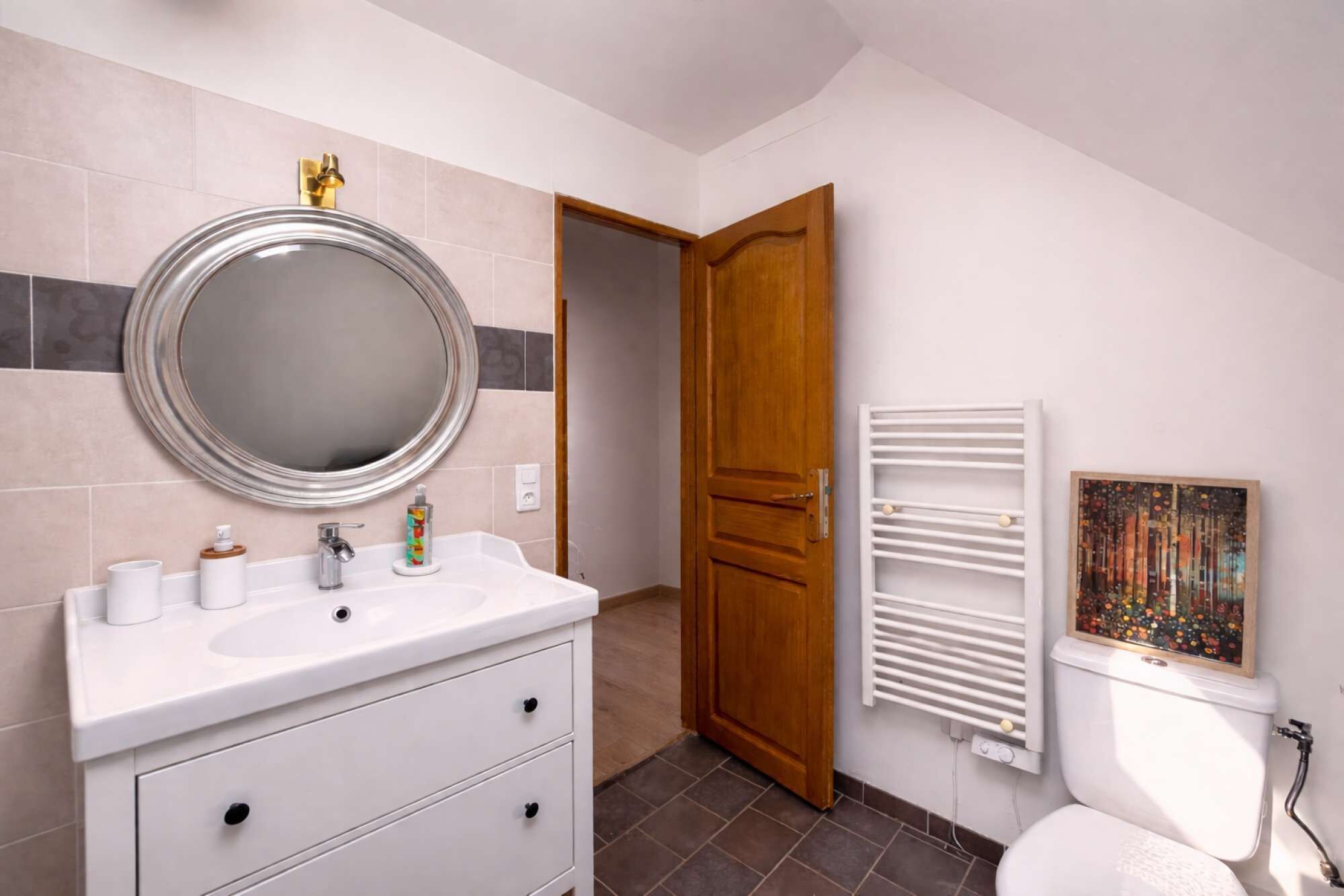 A bathroom with a white sink, mirror, and toilet, a wooden door, and a radiator.