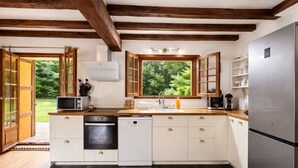 Een keuken met houten balken, een koelkast, een vaatwasser en een raam met uitzicht op groen.