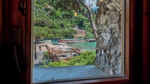 Une vue depuis une fenêtre donnant sur une zone côtière, avec un mur de pierre, une jetée et un bâtiment doté d’un toit rouge.