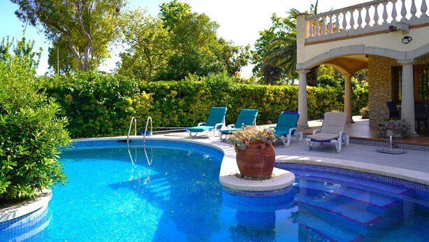 A swimming pool with a tiled edge, surrounded by green hedges and trees. - Spacious villa with private pool near the beach in Costa Brava (Sant Pere Pescador)