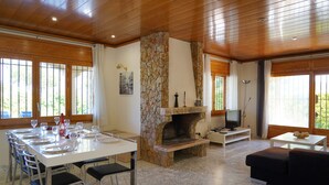 A dining area with a stone fireplace, a television, and a sofa. - Spacious villa with private pool near the beach in Costa Brava (Sant Pere Pescador)