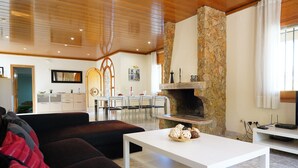 A modern living room with a stone fireplace, a dining area with chairs, and a kitchen in the background. - Spacious villa with private pool near the beach in Costa Brava (Sant Pere Pescador)