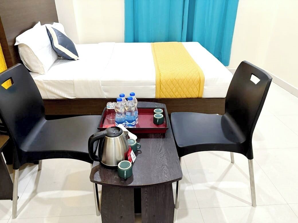 Hotellihuone, jossa on sänky, pieni pöytä, vedenkeitin, kuppeja ja vesipulloja.