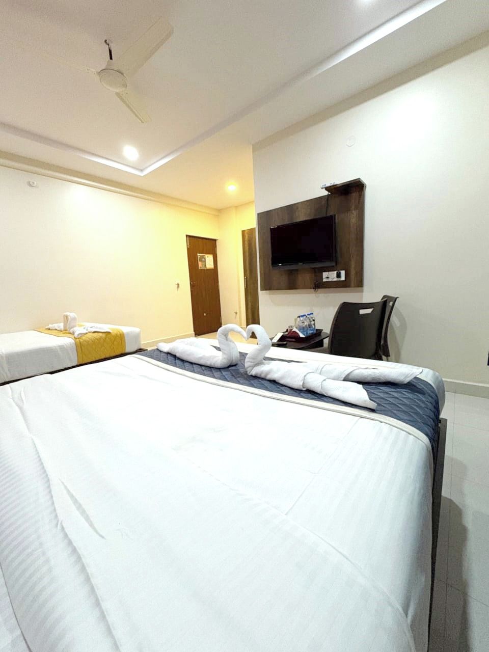 Habitación de hotel con una cama grande, un televisor de pantalla plana en la pared y un ventilador de techo.