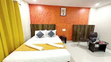 A hotel room with a large bed, a desk with a chair, and a red textured wall.