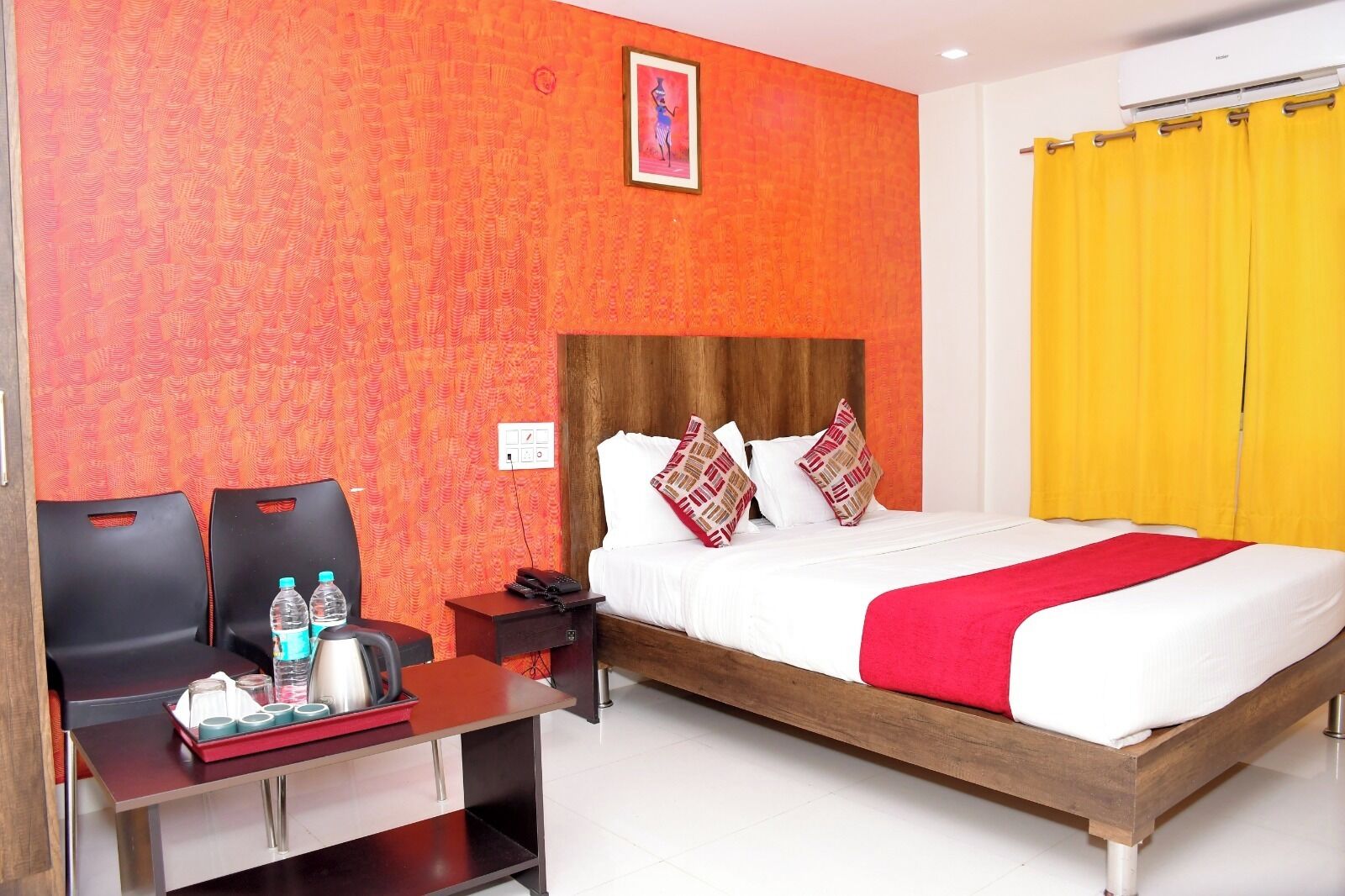 A hotel room with a bed, a desk with chairs, a nightstand, and a wall with a patterned wallpaper.