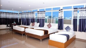 A hotel room with three beds, a desk, and large windows with curtains. - HARSHA COMFORTS (Chikkamagaluru)