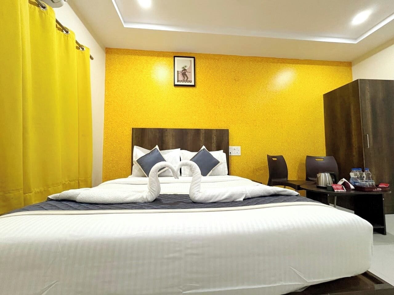 A hotel room with a large bed, a wooden headboard, a desk with a chair, a wardrobe, and a framed picture on the wall.