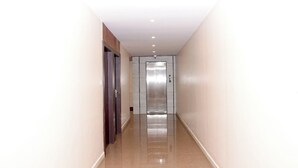 A corridor with a shiny tiled floor, a wooden door on the left, and a metallic elevator on the right. - HARSHA COMFORTS (Chikkamagaluru)