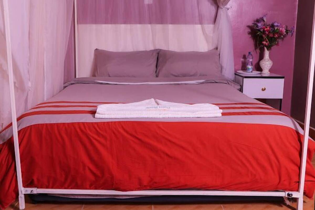 A bed with a canopy, a bedside table with a vase of flowers, and a red and white striped bedspread.
