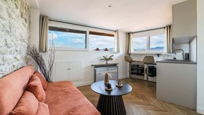 Ein kompakter Wohnbereich mit Sofa, rundem Tisch, Küchenzeile und großen Fenstern mit Blick.