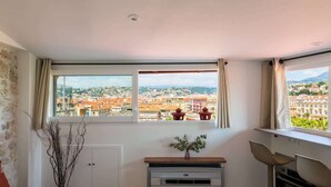 Ein Zimmer mit einem großen Fenster, einer weißen Wand, einem kleinen Schrank und einer Pflanze.