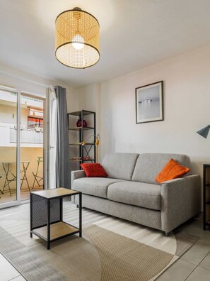 Una sala moderna con un sofá gris, una mesita auxiliar, una lámpara colgante de fibra natural, un cuadro en la pared y vistas al balcón exterior.