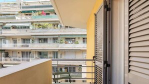 A balcony with a table and chairs, a sliding door, and a view of a multi-story building with balconies. - Studio apartment in the Port of Nice (Niza)