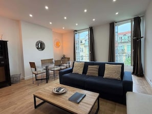A modern living room with a dark blue sofa, a wooden coffee table, and a dining area with chairs and a table.