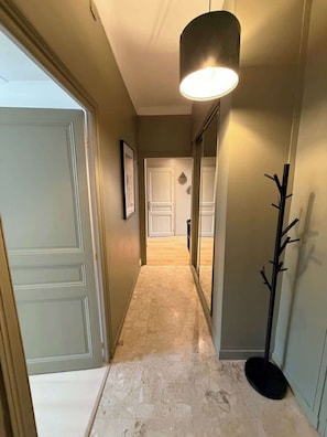 A hallway with a light fixture, a coat rack, and a door leading to another room.