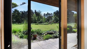 Blick durch eine Glastür in einen Garten mit Rasen, Kübelpflanzen und einem Kiesweg.