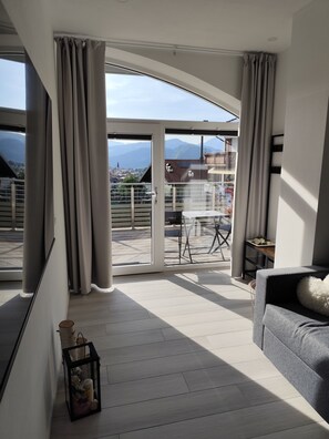 Ein großzügiger Wohnbereich mit Balkon, einem grauen Sofa und einem Tisch mit Stühlen.