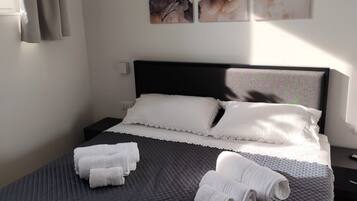 Una cama bien hecha con un edredón oscuro, almohadas blancas y toallas enrolladas sobre un cabecero oscuro.