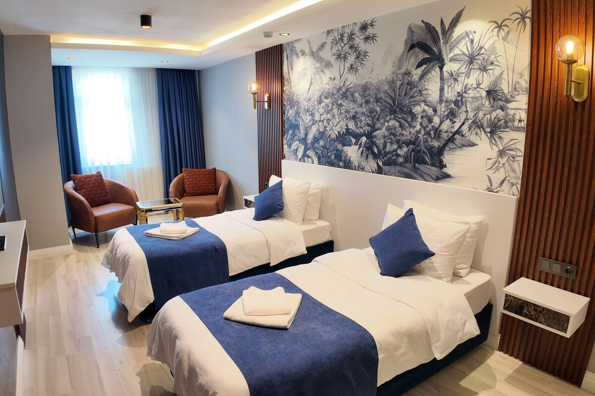 Quarto de hotel com duas camas, televisão, escrivaninha e um mural na parede.