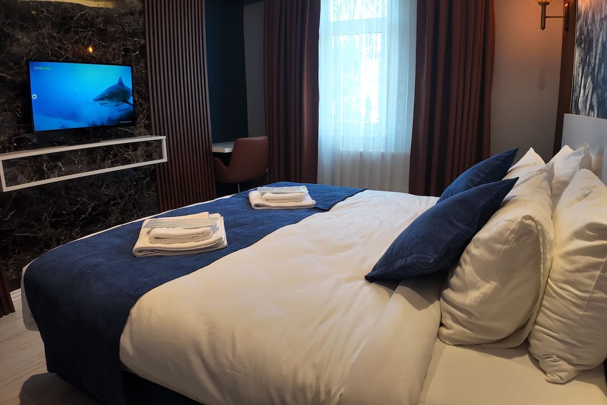 Quarto de hotel com uma cama grande, TV fixada em uma parede de mármore e vista para o exterior pela janela.