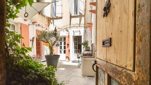 Ein schmaler Gang mit einer Holztür rechts, einem Blumentopf und einem kleinen Tisch mit einem Stuhl in der Mitte.