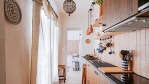 Eine schmale Küche mit Holzschränken, einer schwarzen Arbeitsplatte und hängenden Küchenutensilien.