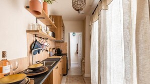 Eine schmale Küche mit Holzböden, einer schwarzen Arbeitsplatte und einem gemusterten Teppich.