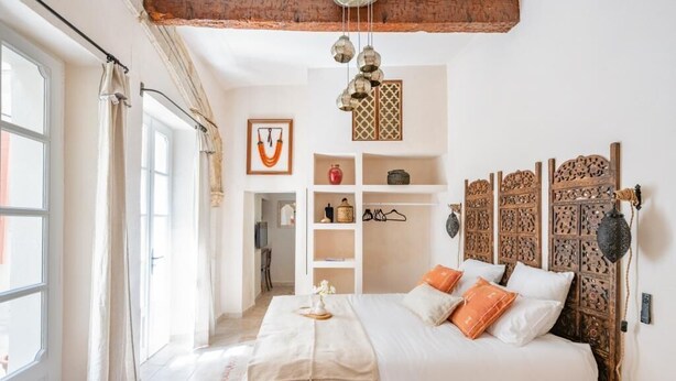 Ein Schlafzimmer mit einem hölzernen Bett, weißer Bettwäsche, einem dekorativen Kopfteil und einer Pendelleuchte.