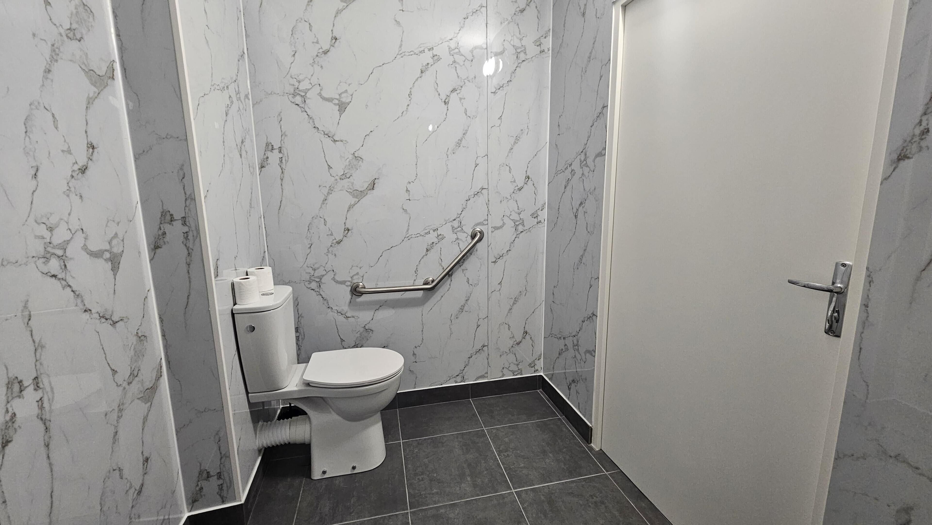 A bathroom with a toilet, a handrail, and a door.