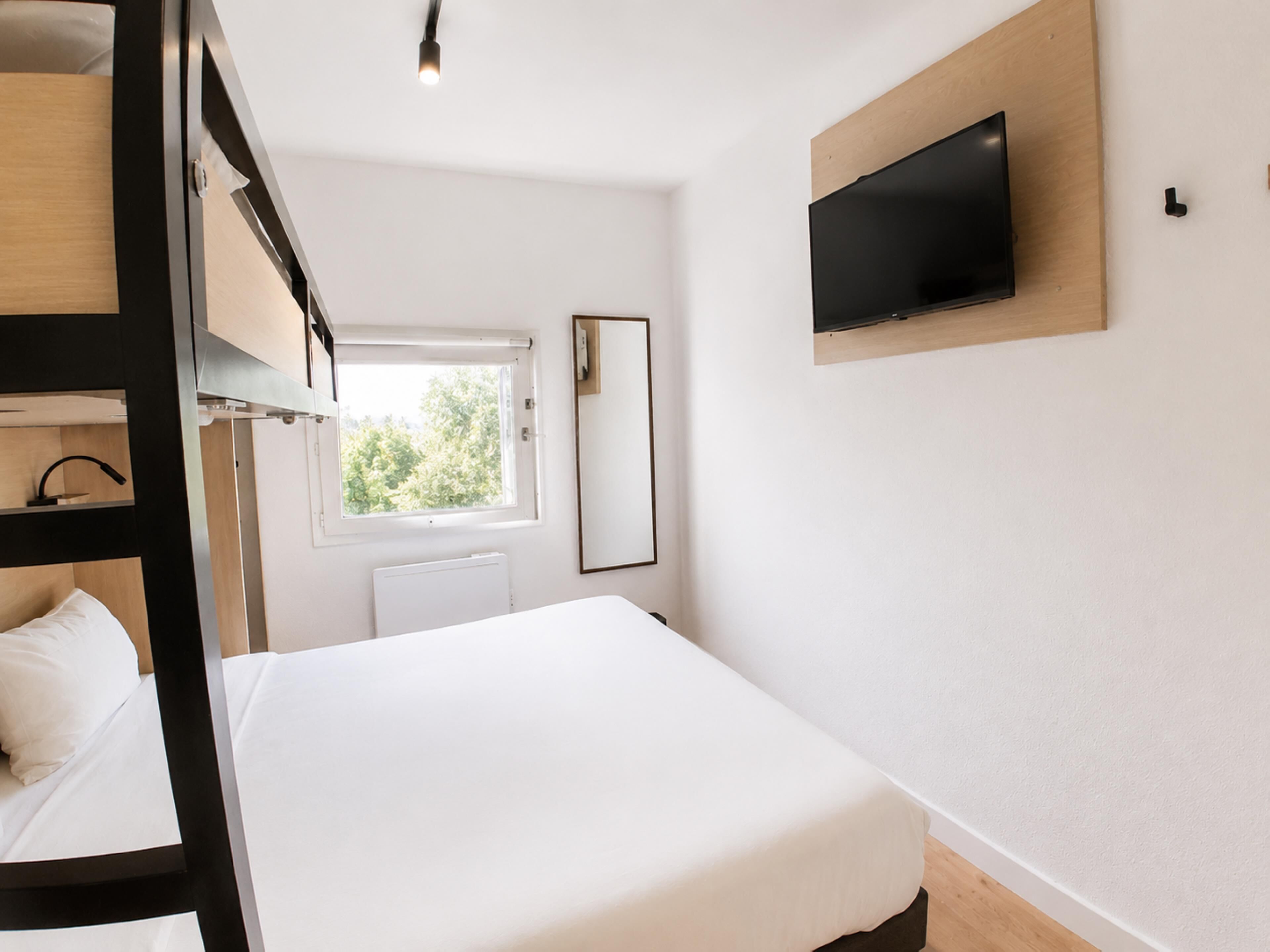 Une chambre d’hôtel avec un lit superposé, un lit simple, un téléviseur fixé au mur et une fenêtre donnant sur un paysage verdoyant.