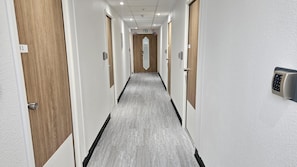 A hotel corridor with wooden doors, a grey floor, and a wall-mounted security keypad. - Kyriad ECO - Tours Nord (Parcay-Meslay)