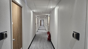 A hotel hallway with doors on both sides, a red bag on the floor, and a fire extinguisher on the right. - Kyriad ECO - Tours Nord (Parcay-Meslay)